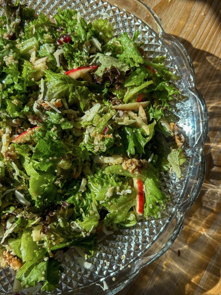 Overhead shot of a harvest grain salad filled with sliced Honeycrisp apples, roasted vegetables, greens, nuts, and dried fruit, all tossed together and drizzled with a maple mustard vinaigrette.