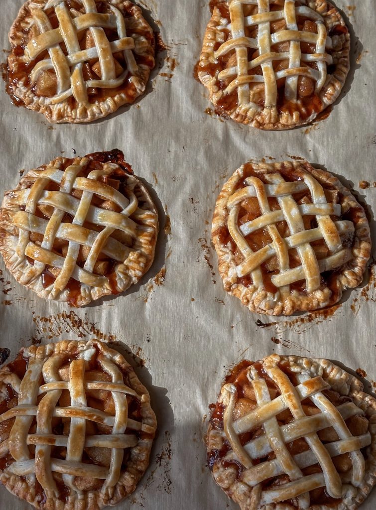 A tray of small, golden-brown mini apple pies with crimped edges and a glossy baked top