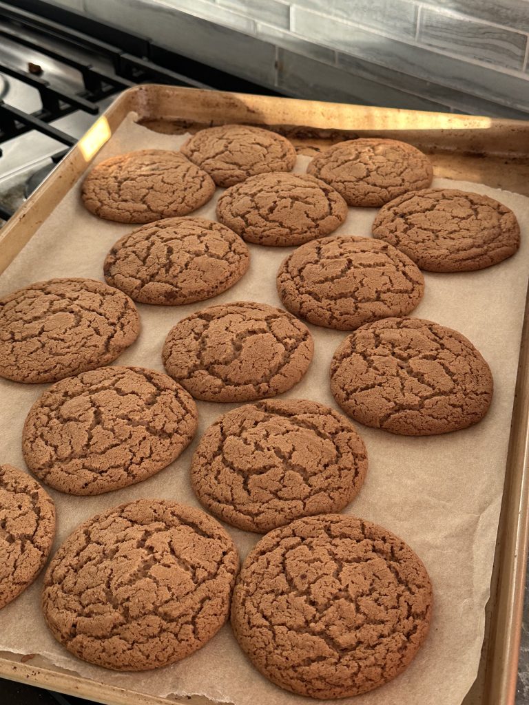 A close-up of homemade brown butter crinkle cookies with crackled, sugar-dusted tops, stacked and slightly overlapping on a baking surface, showing their rich golden-brown color and soft, fudgy centers.