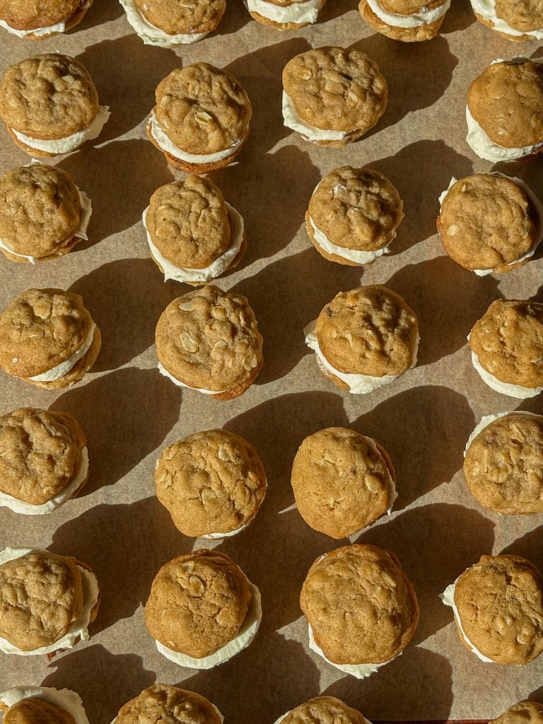 Close-up of mini oatmeal cream cookies stacked on a plate, showing soft oatmeal cookies sandwiched with a swirl of vanilla cream filling in warm natural light.