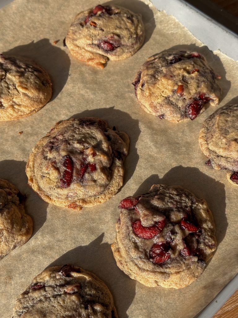 Close-up of a cherry chocolate cookie with visible chunks of melted chocolate and pieces of cherry, showing a soft, chewy center and crisp edges.
