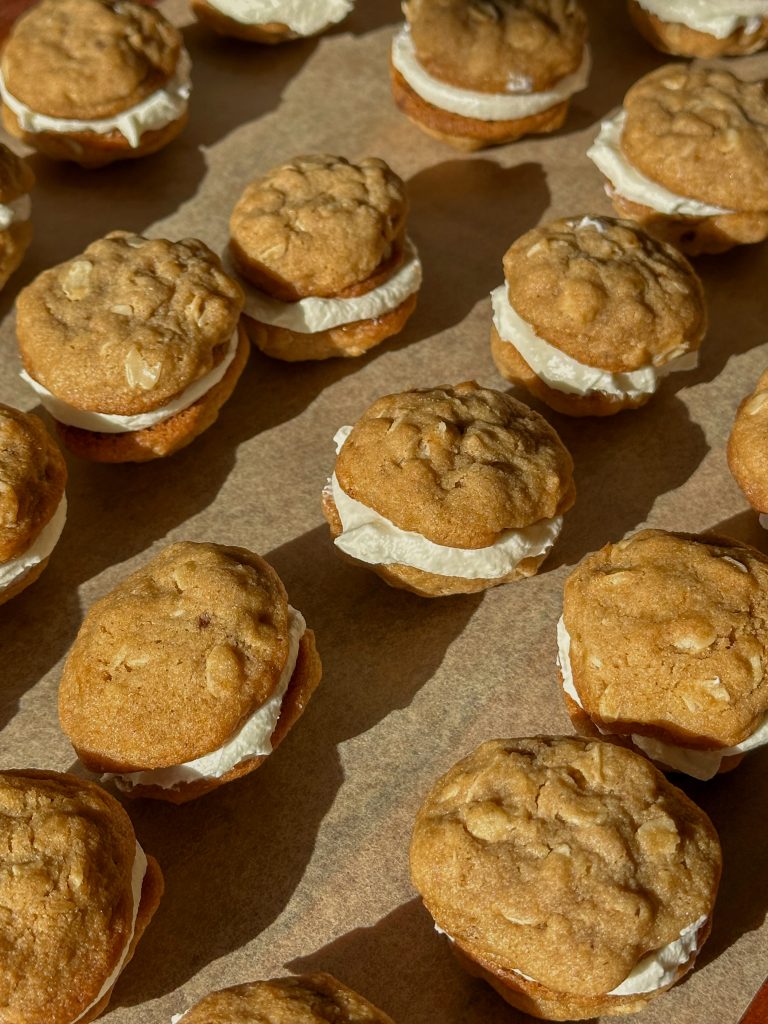 Close-up of mini oatmeal cream cookies stacked on a plate, showing soft oatmeal cookies sandwiched with a swirl of vanilla cream filling in warm natural light.
